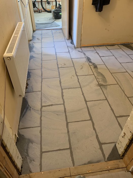 Fogat hallgolv med nya kakelplattor och synlig fogmassa i arbetsprocess.