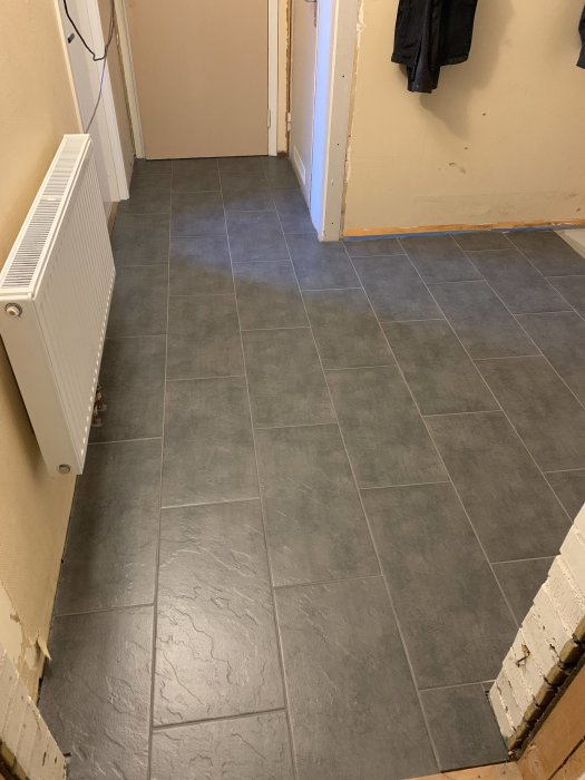 Nyfogat hallgolv med gråa klinkerplattor och synlig värmeelement till vänster.