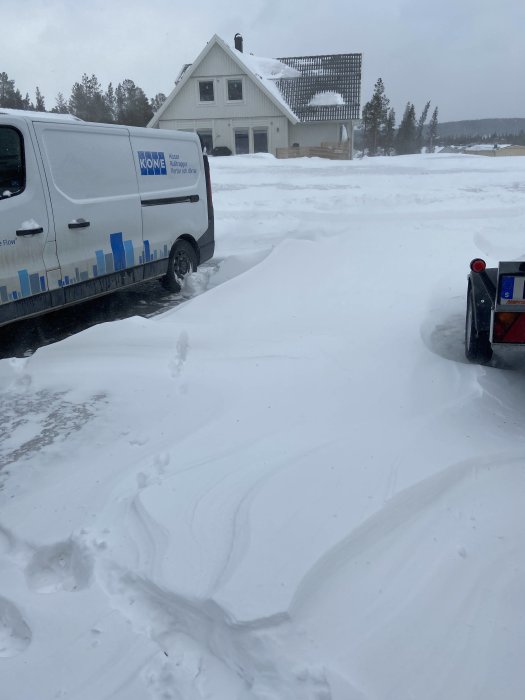 Snötäckt uppfart med en skåpbil och en husvagn framför ett hus.