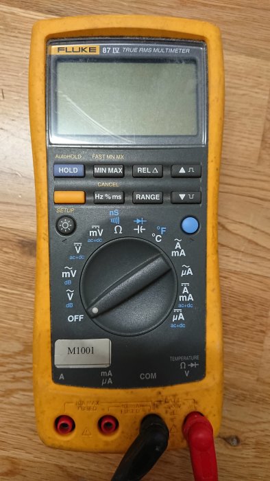 Multimeter av märket Fluke 87 IV på en träyta med svarta och röda mätprober anslutna.