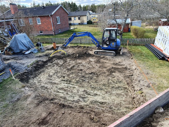 Grävmaskin vid utgrävningsarbete för fundament till garage med synliga el- och vattenledningar.