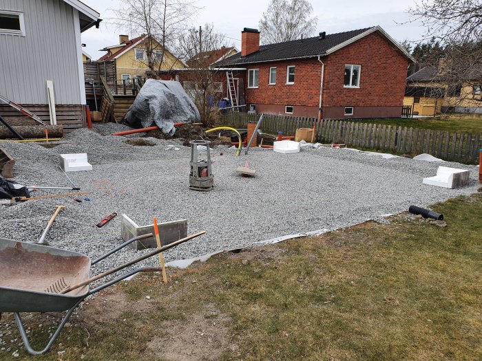 Grävning med grus och kantelement för garage med byggmaterial och verktyg på gården.