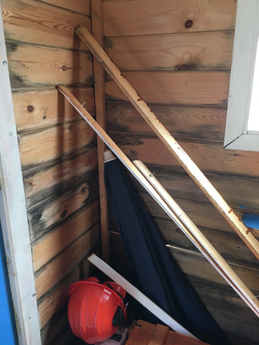 Verktygsbodens inre hörn med mögelspår på träväggar och en synlig röd hjälm samt verktyg på hyllan.