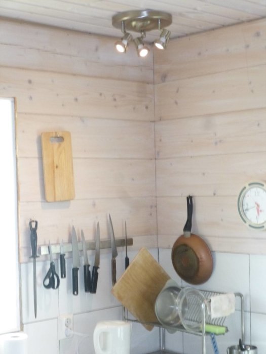 Spotlightsarmatur monterad i hörn över köksbänk med knivlist och hängande köksredskap.