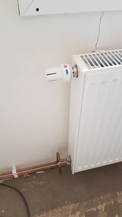 Radiator ansluten till kopparledningar med termostatventil vid en vit vägg.