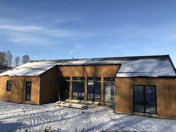 Nybyggt hus med värmebehandlad furupanel under vintersäsong, snö på taket.