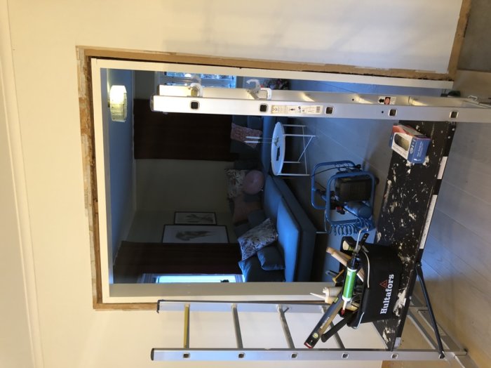 Bild på ett vardagsrum under renovering med en stege och renoveringsverktyg, synliga väggstrukturer och valvet är färdigt.