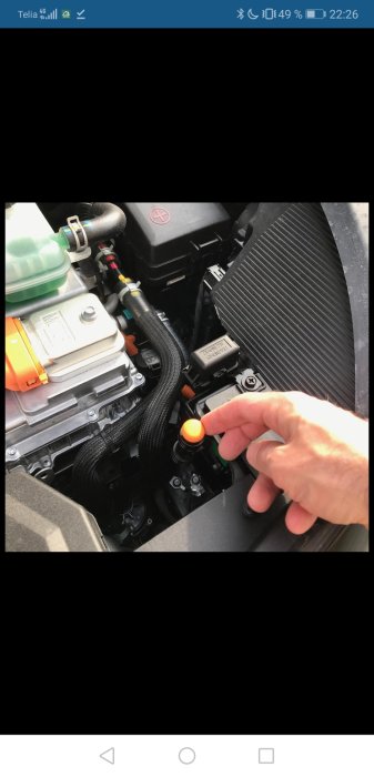 Hand pekar på en orange nödutlösare i en bilens motorrum.