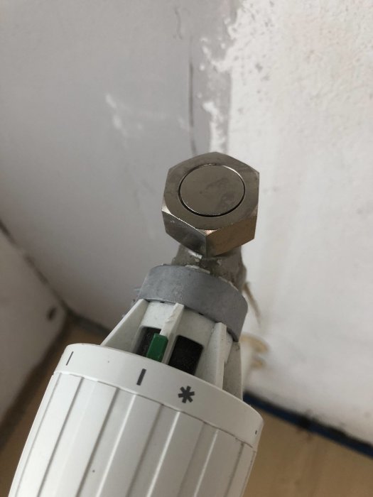 Demonterad termostatventil med synlig mutter och pluggat rör mot vit vägg.