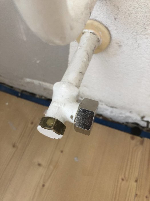 Demonterad vit vattenledning med pluggad ände nära en vägg och golvsockel.