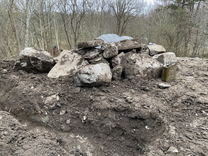 Grund utgrävd för växthus med en stor hög av sprängsten på jordig mark.