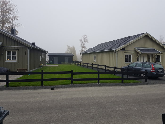 Liggande två-plankstaket i svart som terrasseras ned längs en gata med enfamiljshus och varierande marknivåer.