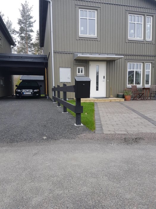 Nylagd terrasserad trädgårdsstaket av mörkt trä framför hus med bil i carport.