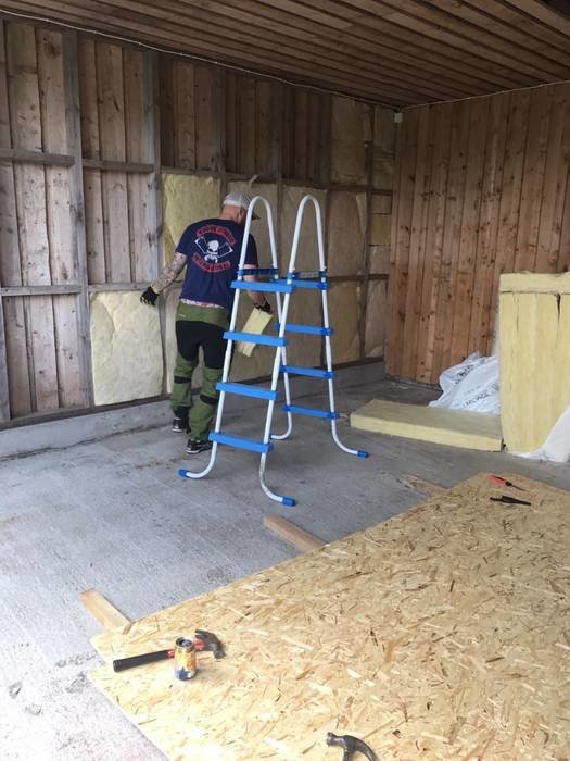 Person som isolerar en vägg i en carport ombyggd till gym, isolering och verktyg syns.