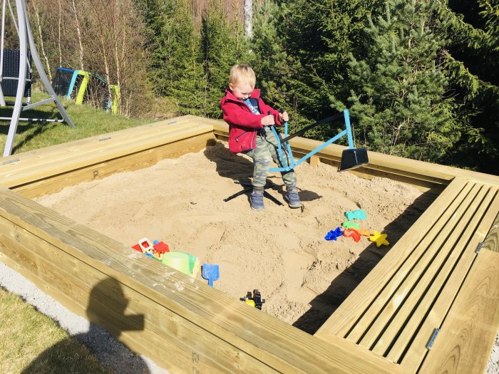 Barn leker i en nyfylld sandlåda med två kärror sand och leksaker.