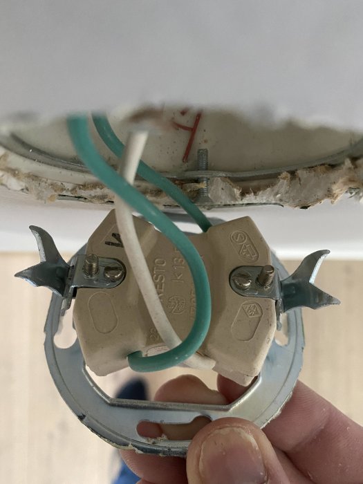 Närbild av en gammal trappströmbrytare med två gröna kablar och en vit kabel fastskruvade, mot en vit vägg.