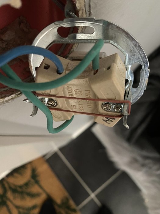 Öppen eldosa med gammal trappströmbrytare och trådar i grönt och blått mot en tegelvägg.