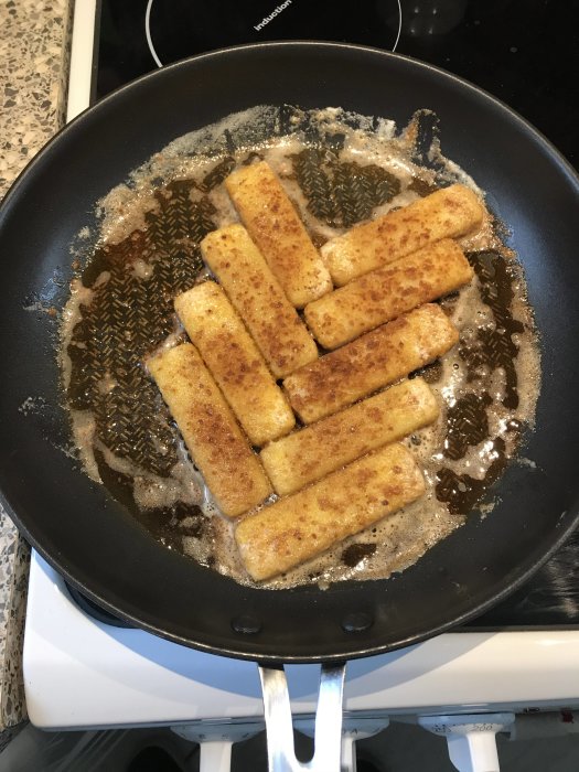 Stekpanna med fräsande fiskpinnar på spisen.