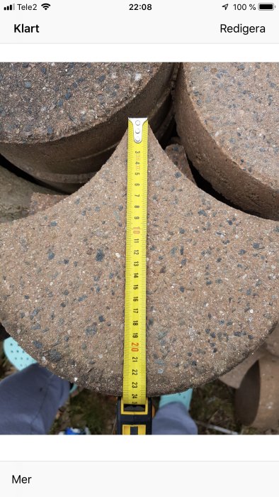 Måttband visar dimensioner på brun trädgårdsplatta, ca 23 cm, i utomhusmiljö.