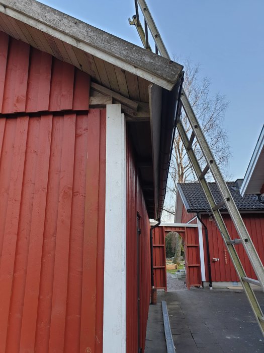 Rödmålat hemmagym i carport med öppet tak och tillfällig lösning, stege lutad mot byggnaden.