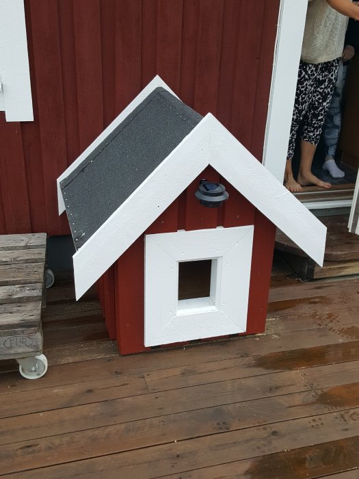 Handbyggt rött katt hus i trä på en veranda, designat som ett miniatyrhus.