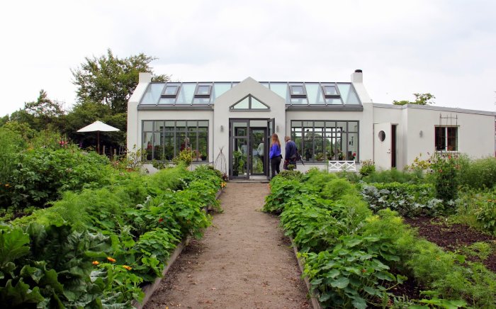 Ett växthus med angränsande grönsaksland och två personer som går mot ingången.