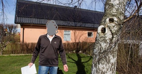 Hus med solceller på taket, man med suddat ansikte framför och stort träd till höger i bild.