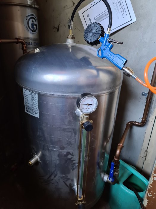 Vattentank ansluten till kompressor och mätare i en pannrumsmiljö.