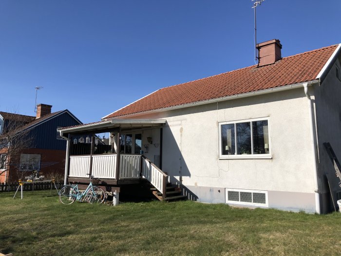 Nybyggt trädäck med staket kopplat till husets altan, grön gräsmatta och cyklar framför.