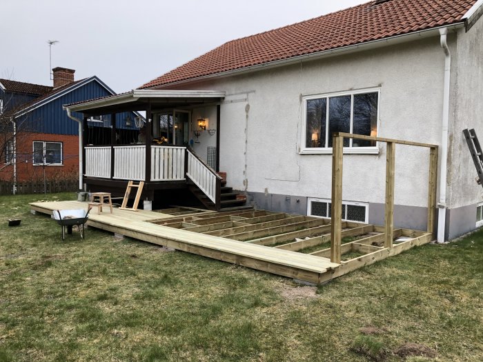 Nybyggt trädäck under konstruktion bredvid en befintlig altan vid en husfasad.