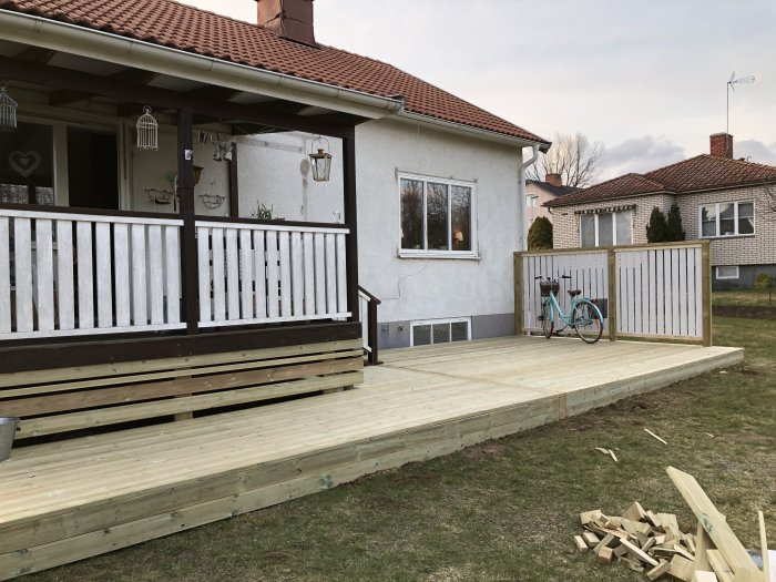Nybyggt tralläck med staket vid hus med befintlig altan, gräsmatta och cykel.