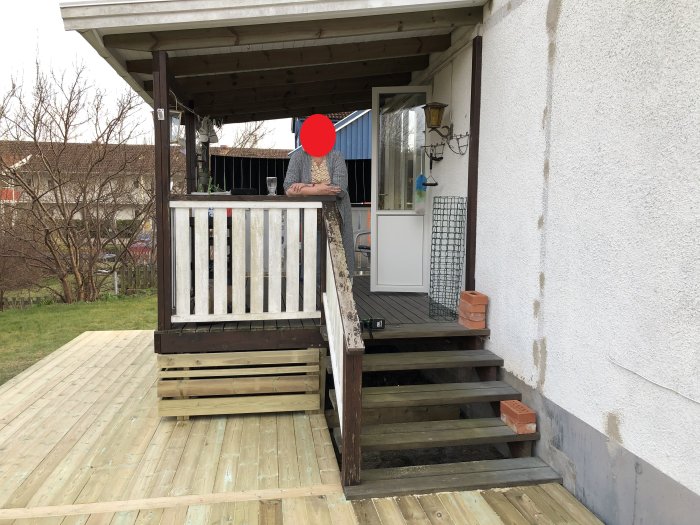 Nylagd trall och renoverad altan vid hus med delvis synlig person som lutar sig på räcket.