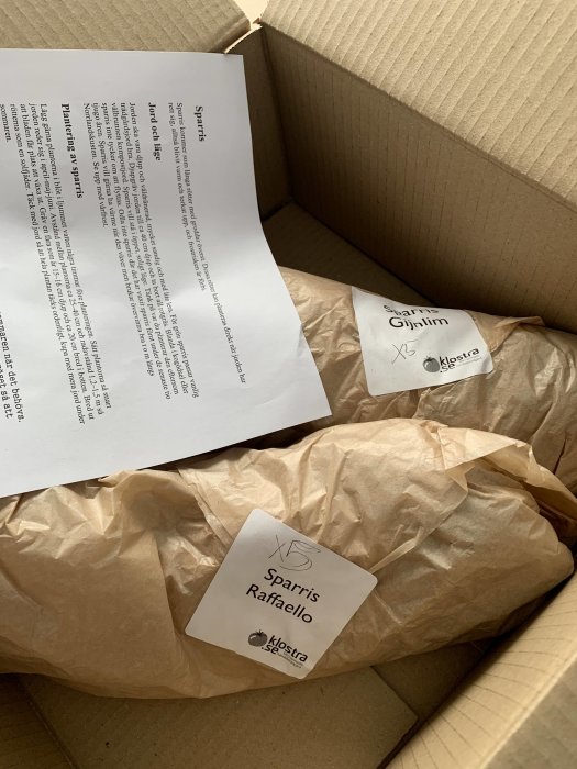 Öppen kartong med ett paket markerat "Sparris Raffaello" och ett blad med planteringsinstruktioner.