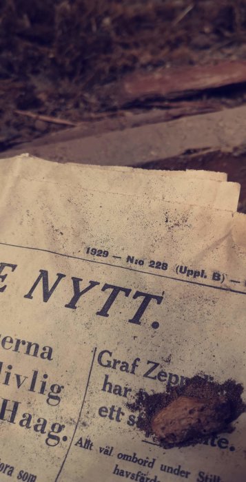 Gamla tidningssida från 1929 med texten "NYTT" synlig, delvis täckt av jord och byggavfall.