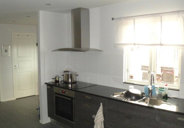 Kök med 30x60cm kakel på högkant och fläkt ovanför köksbänk vid fönster.