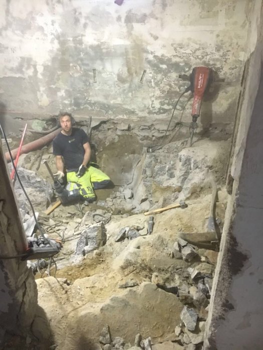 Person som arbetar med källarrenovering, omgiven av sten och byggutrustning med synlig gammal golvnivå.
