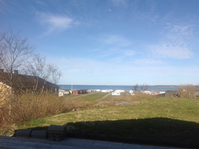 Utsikt över en campingplats vid havet, med husvagnar och grönområden under en klar blå himmel.