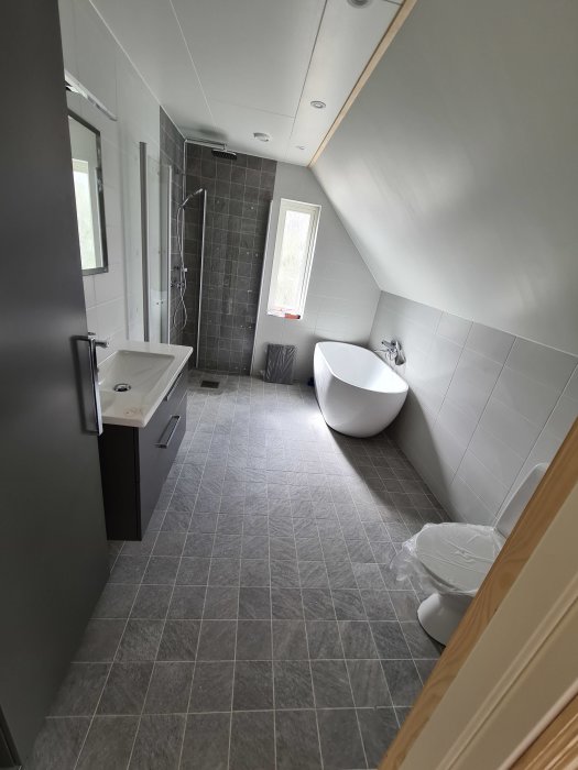 Modernt badrum med gråa klinkergolv, fristående badkar, duschkabin och handfat.