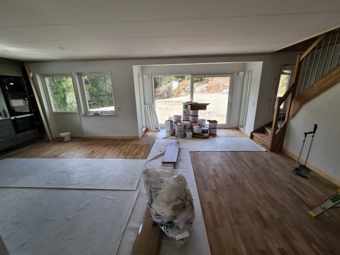 Inredning av ett hus under renovering med trägolv, fönster, en trappa och byggmaterial.