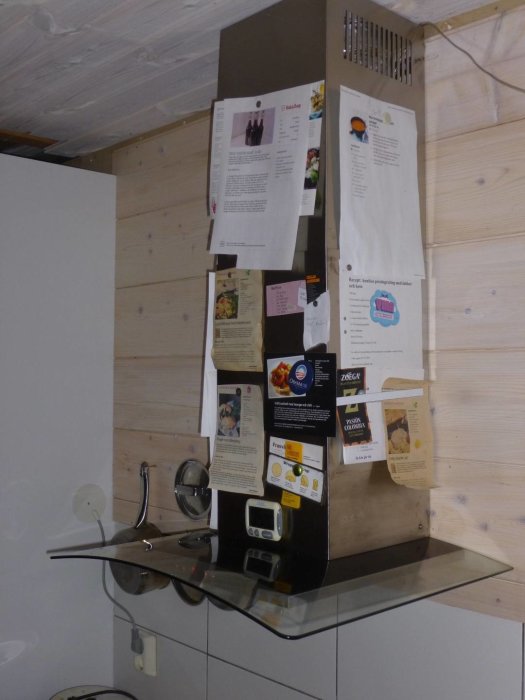 Kök med kakelstänkskydd, vitvaxad träpanel och köksfläkt, utsmyckad med recept och notiser.