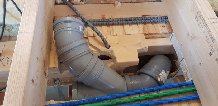 Installation av gråa avloppsrör och blåa samt gröna rör för vatten i en träregelstomme.