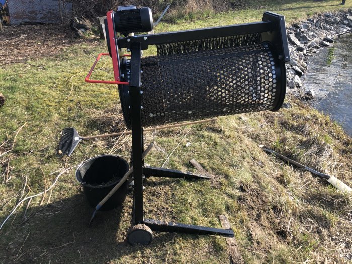 Sålltrommel för trädgårdsarbete vid strand med hink, kratta och våt sand runtomkring.