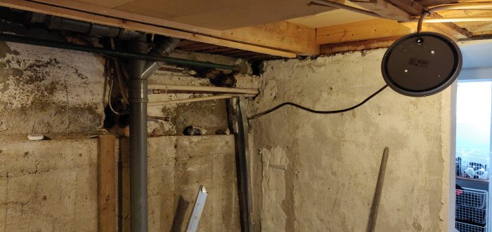 Delvis exponerad bärande källarvägg med synliga rör och träbjälklag som är part of en diskussion om väggavlägsning.