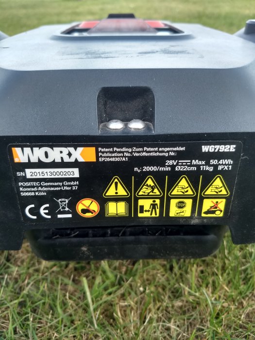 Närbild på en Worx landroid L (WG792E) robotgräsklippares etikett med serienummer och varningssymboler.