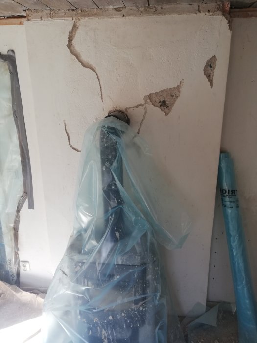 Renoveringsprojekt visar en murstock med synliga sprickor och lossnar delar, täckt av byggnadsplast.