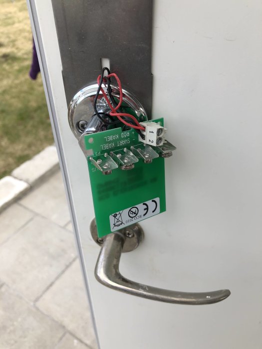 Öppen bakdörr till garaget med ett synligt kretskort och anslutna kablar runt dörrhandtaget.