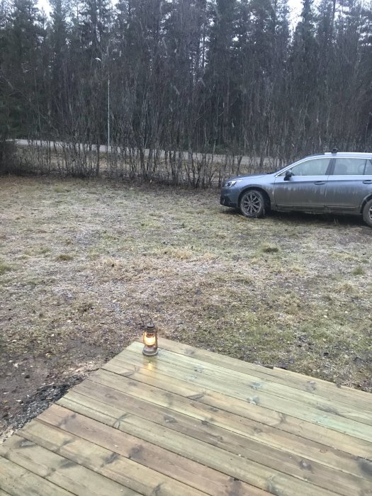 Träkoja under konstruktion med obehandlad träfasad, vid en gräsmark nära parkerad bil och skogsbryn.