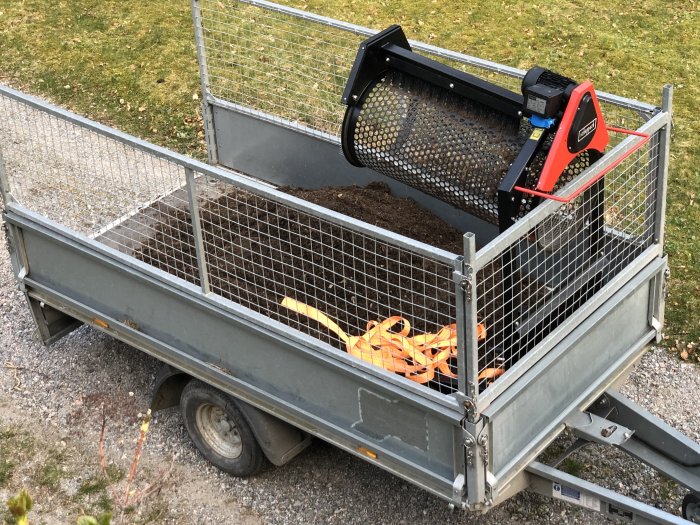 Jord i en släpvagn med en svart och röd trumblandare och några verktyg på sidan.