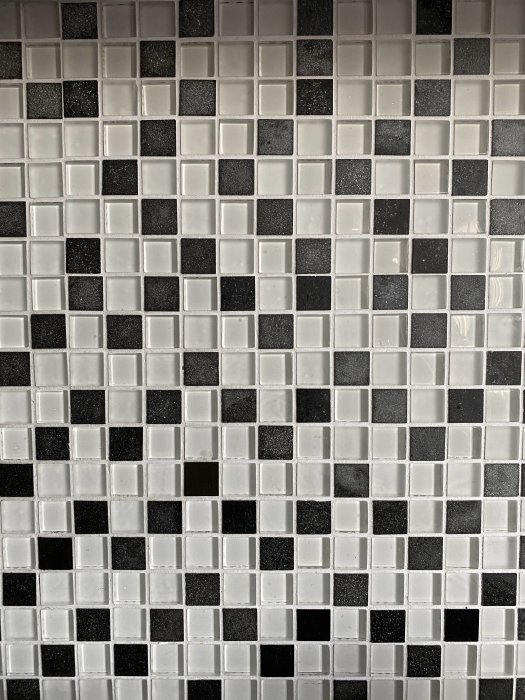 Svartvit kvadratisk mosaik på vägg, potentiellt för köksrenovering.