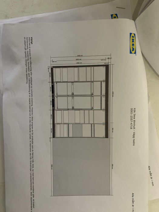 Ritning av köksskåpslayout från IKEA med måttangivelser, placerad på en bordsskiva.